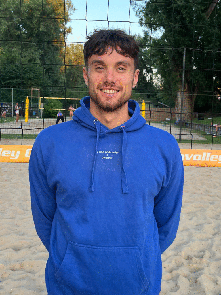 BSC Webdesign Athlete Michael Kessler mit blauem Hoodie am Beachvolleyballfeld bei Sonnenuntergang.