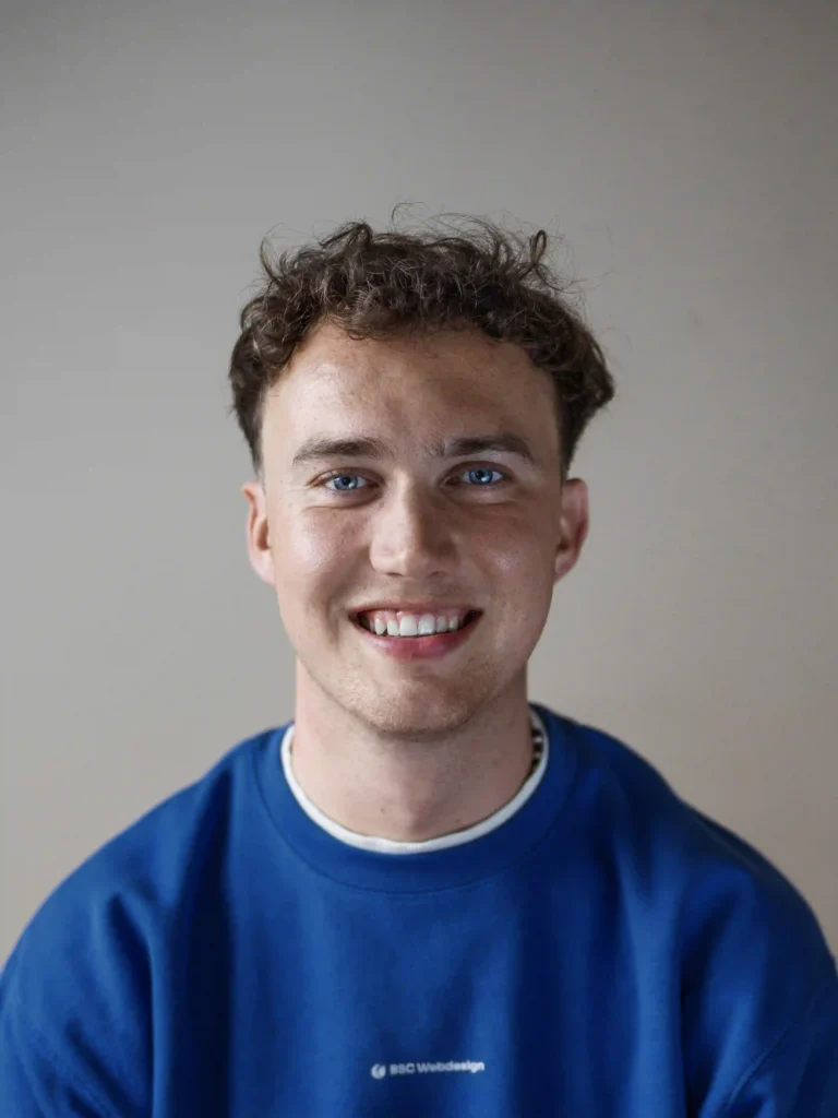 Porträt von Aaron Csok, junger Mann mit kurzem Haar und blauem BSC-Pulli Hemd, lächelt freundlich in die Kamera.