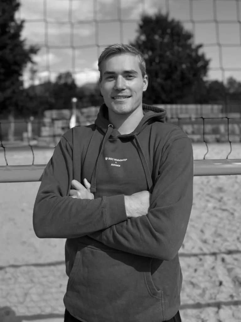 BSC Webdesign Athlete Daniel Ritzer im schwarz-weißen Portrait mit Hoodie am Beachvolleyballfeld.