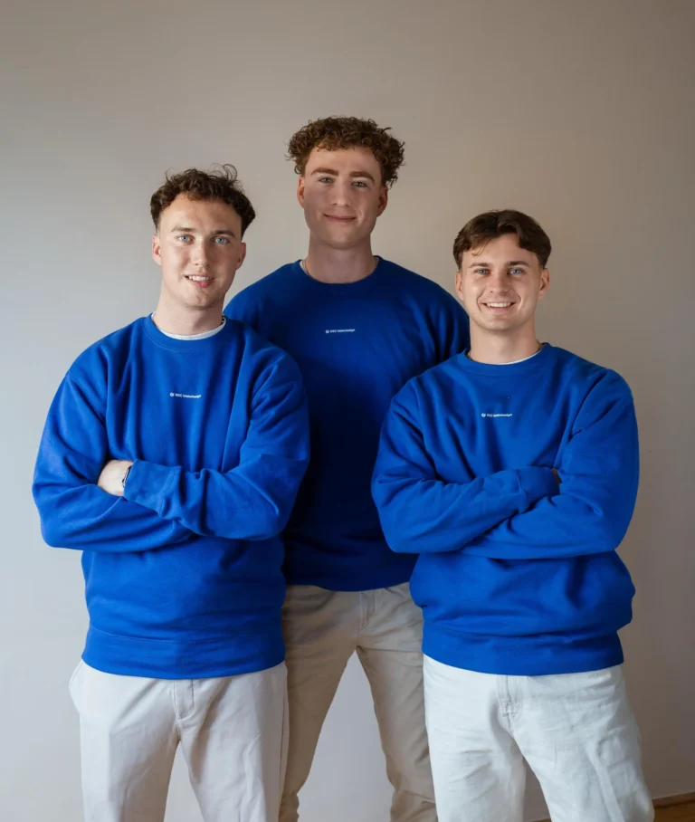 Die drei Teammitglieder von BSC Webdesign stehen nebeneinander in blauen Pullovern vor neutralem Hintergrund.
