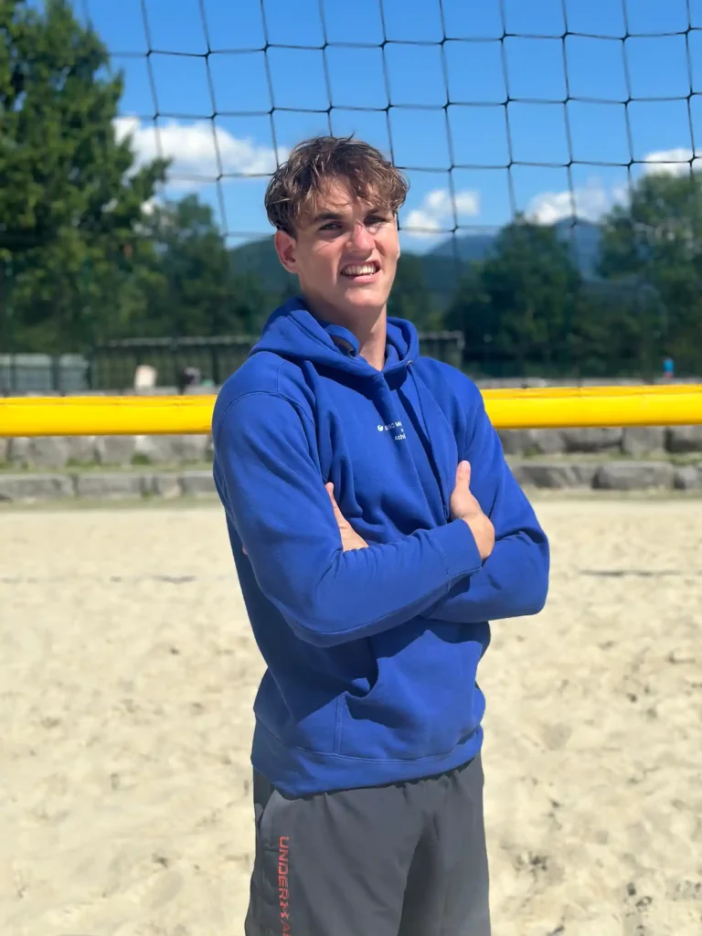 BSC Webdesign Athlete Tobias Wallner mit blauem Hoodie am Beachvolleyballfeld bei Sonnenuntergang.