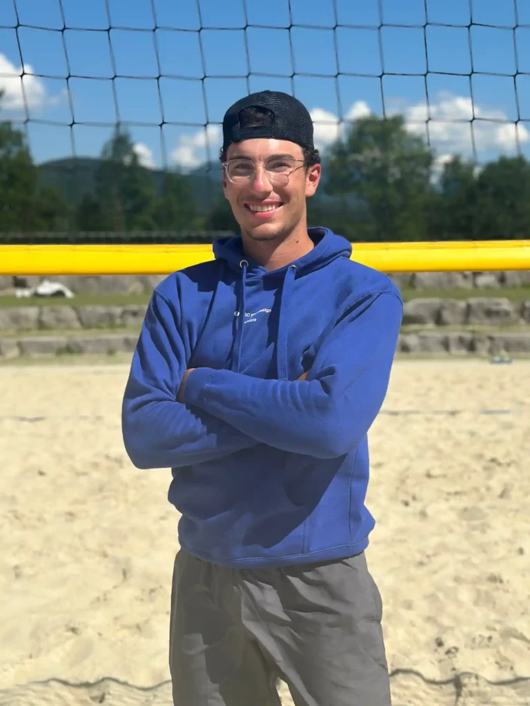BSC Webdesign Athlete Valentin Stöllinger mit blauem Hoodie am Beachvolleyballfeld bei Sonnenuntergang.